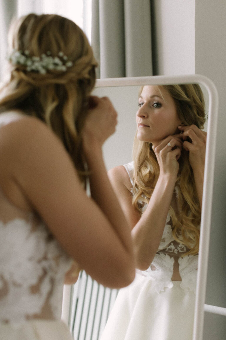 Die Braut beim anziehen der Ohrringe vor dem Spiegel