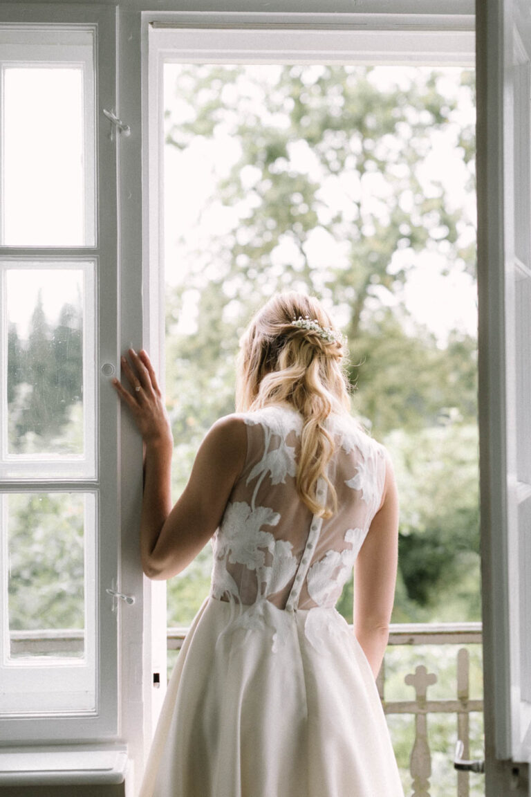 Die Braut lehnt im Fensterrahmen und blickt nach draussen, Hochzeit Gut Sonnenhausen - Alexandra Kasper