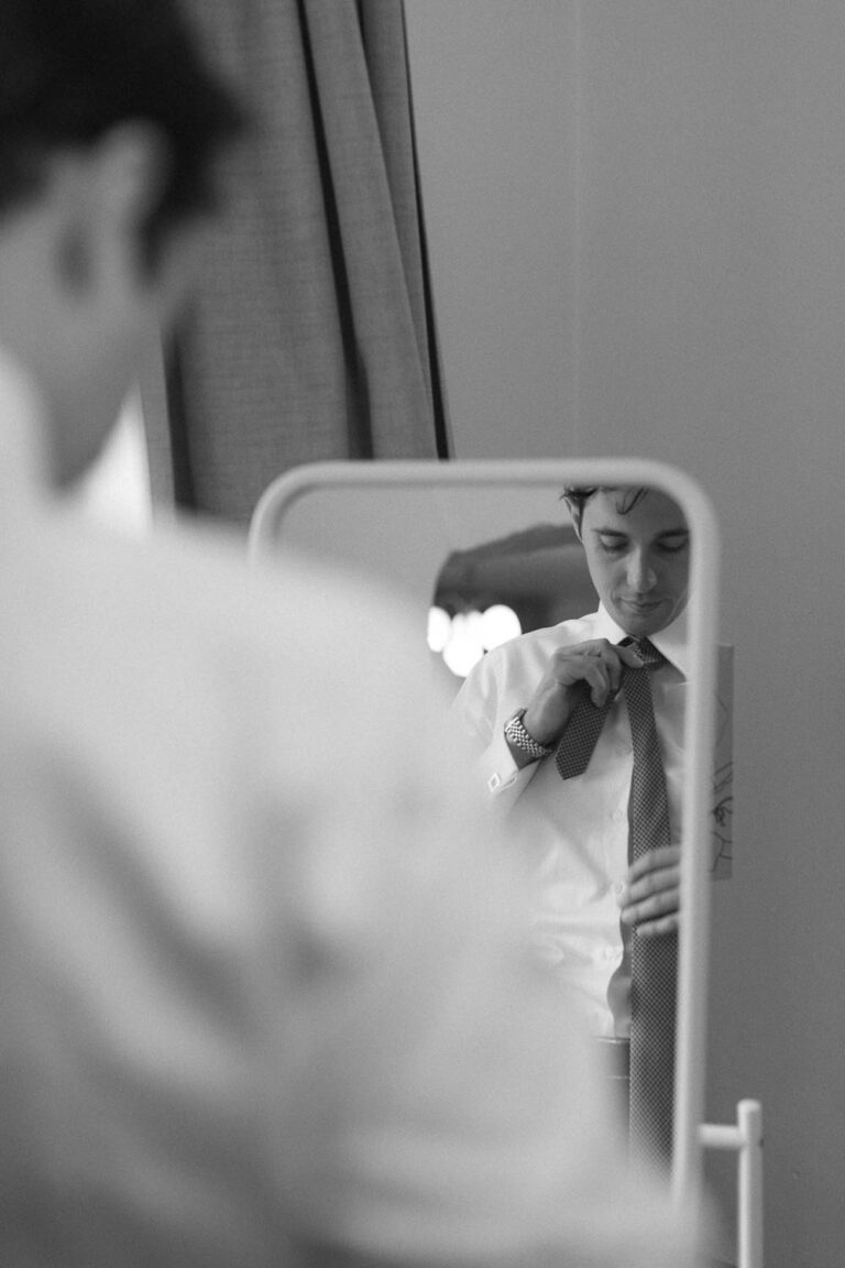 Portrait vom Bräutigam beim anlegen der Krawatte vor dem Spiegel, Hochzeit Gut Sonnenhausen - Alexandra Kasper
