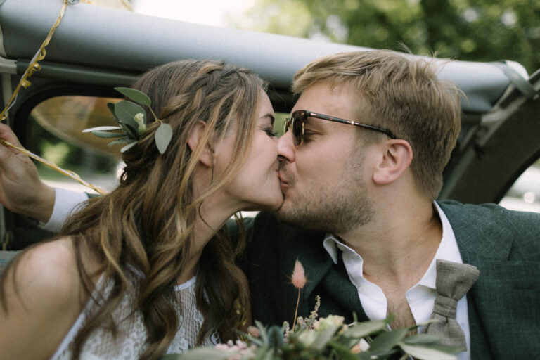 Das Hochzeitspaar küsst sich im Auto vor dem Standesamt in München